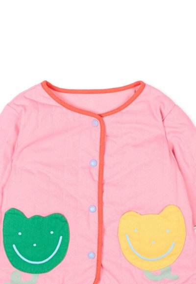 Vêtement pour bébé à manches longues rose avec bordure rouge, boutons-pression sur le devant, et patchs de visages souriants verts et jaunes sur les côtés inférieurs.