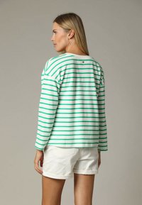 Pull-over rayé vert et blanc avec des manches longues, tissu texturé, et encolure ronde. Un short blanc avec des ourlets retournés est porté.