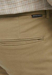 Khaki pants with a smooth texture, featuring a piped back pocket and a black label with "JACK & JONES" on the waist.