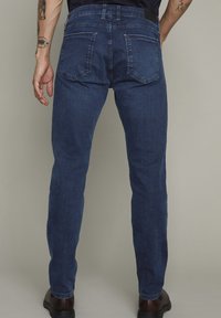 Tmavě modré džíny s rovný fit, pěti kapsami a viditelnými švy. Pas má smyčku na opasek.