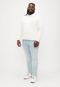 Fehér pulóver, polo gallérral, világoskék, slim-fit farmer és fehér sportcipő barna akcentussal. Egyszerű, lazán elegáns öltözet.