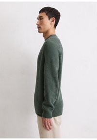 Pulover verde din tricot cu dungi, decolteu rotund, maneci lungi și o croială lejeră. Asortat cu pantaloni din catifea cu nuanță off-white.