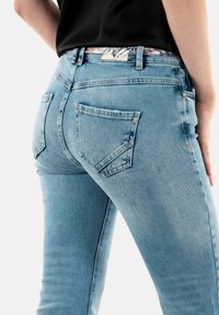Jeans in denim azzurro chiaro con vita a media altezza, dotati di una cintura con motivo floreale, due tasche posteriori e un design slim fit.