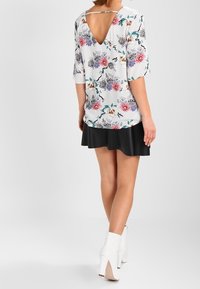 Top con motivo floreale e scollo a V, con maniche corte e base bianca. Abbinato a una gonna nera a campana e stivaletti bianchi con tacco.