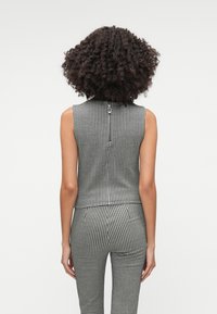 Schwarz-weißes Hahnentrittmuster ärmelloses Top mit hohem Kragen und Rückenreißverschluss. Der Stoff hat eine glatte Textur.