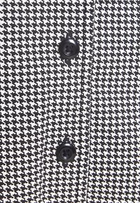 Svartvitt houndstooth-mönstrat tyg med en blank svart knapp. Texturen verkar slät med ett skarpt, kontrasterande mönster.