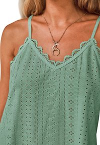 Mintgroene camisole met kant trim, voorzien van uitsparingspatronen en kleine diamantvormige figuren. Een gelaagde ketting met hangeraccenten is zichtbaar.