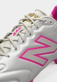 Chaussure de sport blanche avec logo "N" rose, lacets beiges, "442" en rose sur la languette, et texte doré "New" près du haut.