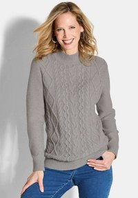 Grauer Strickpullover mit strukturiertem Zopfmuster, gerippten Bündchen und Saum, hochgeschlossenem Kragen und taillierter Passform. Getragen mit blauen Jeans.