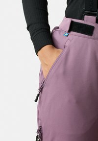 Paarse outdoor broek met verstelbare banden, zijzakken en een klein Zweeds vlagdetail op de tailleband. Glad materiaal, aansluitend ontwerp.