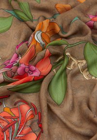 Foulard floreale con uno sfondo marrone decorato da fiori intricati arancioni, rosa e verdi, che presenta una texture morbida e colori vivaci.
