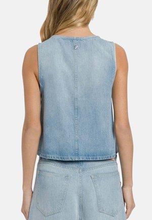 Frau von hinten gesehen, trägt hellblaues ärmelloses Denim-Top und passende Denim-Hose vor einfarbigem Hintergrund.