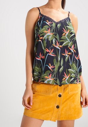 Kobieta ubrana w czarną kwiecistą koszulkę na ramiączkach z koronkową lamówką oraz mini spódniczkę z zamszu w kolorze musztardowej żółci, zapinaną na guziki z przodu.