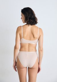 Set di lingerie in beige chiaro composto da reggiseno e mutande a vita alta, con una leggera lucentezza, spalline regolabili e texture senza cuciture, visto da dietro.