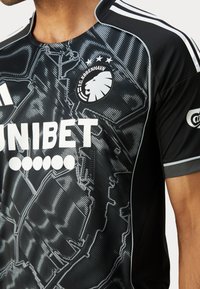 Svart sportsdrakt med teksturert mønster, med hvit "UNIBET" logo, FC København emblem, og tre stjerner. Utsmykket med grå detaljer.