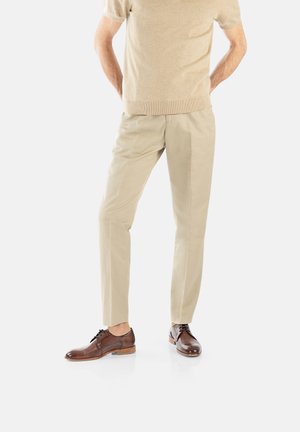 Beige Baumwollhosen mit einer lockeren Passform, kombiniert mit braunen Leder-Schnürschuhen mit glatter Textur und kontrastierender Sohle.