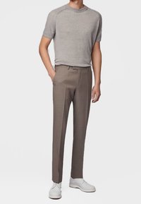 Szary, krótki sweter z dzianiny w zestawieniu z jasnobrązowymi, dopasowanymi spodniami i białymi tenisówkami. Gładka tkanina o dopasowanym kroju.