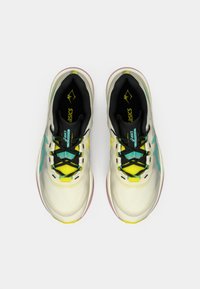 Világos színű futócipők fekete részletekkel, sárga akcentusokkal, texturált felsőrésszel és párnázott talppal. A fűzők különböző színek keverékéből állnak.