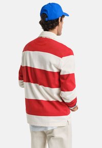 Rood- en witgestreepte lange mouwen shirt met een kraag, gemaakt van katoen. G gedragen met een blauwe pet en lichte broek.