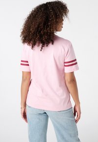 Roze katoenen t-shirt met korte mouwen, voorzien van twee kastanjebruine strepen op elke mouw. Ontspannen pasvorm, zichtbare stikseldetails en een effen achterkant.