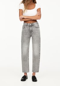 Jeans de mezclilla grises de talle alto con un corte recto, que cuentan con bolsillos delanteros y una textura desgastada. Combinados con una blusa blanca ajustada y mocasines negros.