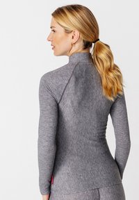 Graues Langarmoberteil aus strukturierter Stretchstoff mit Stehkragen, schmaler Passform und kleinem roten Logo am unteren Saum.