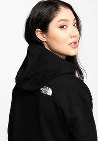 Sudadera con capucha negra hecha de algodón suave, con un logo blanco en el hombro. El diseño incluye una capucha prominente y un corte relajado.
