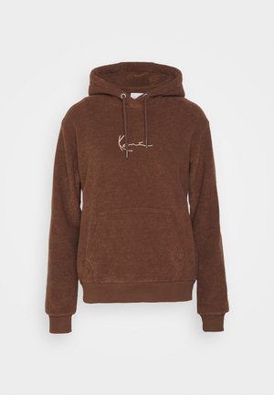 Ruda kapučinė palaidinė pagaminta iš tekstūrinio audinio, turi priekinę kišenę ir raištelius. Išsiuvinėtas logotipas šviesesnės spalvos.