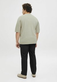 Chemise en coton vert clair à manches courtes, avec une coupe décontractée et une texture côtelée, associée à un pantalon noir et des chaussures décontractées beiges.