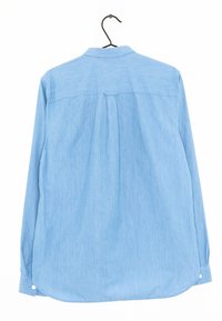Jasnoniebieska, długorękawowa koszula wyeksponowana tyłem na wieszaku. Posiada kołnierz zapinany na guziki, tylną yoke oraz zaokrąglony dół z guzikowymi mankietami.