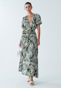 Maxikleit rohevalge ja rohelise palmilehe mustriga, lühikeste paeltega varrukatega, paelaga piheldatud vöökohaga ja lendleva siluetiga.