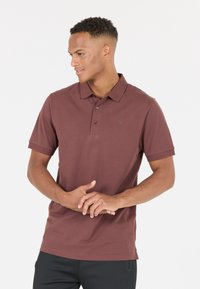 Mörkröd polo skjorta med korta ärmar och krage. Har tre knappar och en diskret logotyp på bröstet. Slät textur.