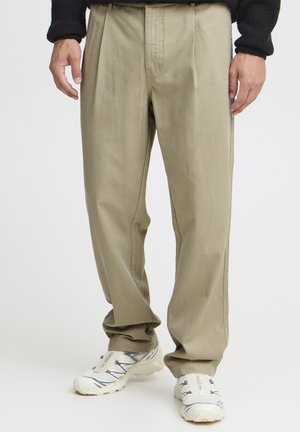 Beige pleated trousers made of lightweight fabric, featuring a straight cut and side pockets, paired with white sports shoes.