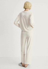 Tricou lung cu maneci crem deschis si pantaloni largi asortati. Material moale cu o textura neteda. Încălțămintea constă în papuci gri, ușor de încălțat.