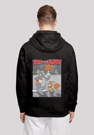 Svart hettegenser med et fargerikt grafisk motiv av Tom og Jerry som spiller basketball, med tegneseriefigurer og oransje basketballer mot en grå bakgrunn.