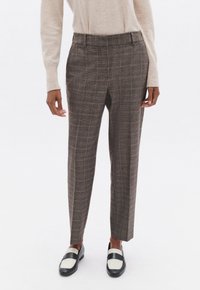 Pantalones de cuadros marrones con un corte entallado, que cuentan con una cintura alta y pliegues marcados, combinados con mocasines en blanco y negro.