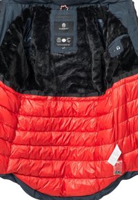 Svart fuskpälsfoder och röd quiltad isolering inuti jackan, med etiketter på insidan och ett slätt yttermaterial.