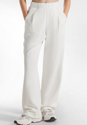 Pantaloni largi albi cu pliuri în față și talie elastică, asortați cu adidași ușori. Material neted, design casual.
