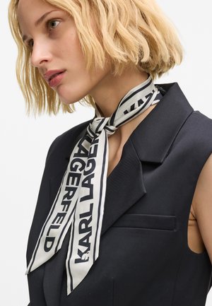 Hvit silke skjerf med svart tekst, knyttet rundt halsen. Teksten viser merkevarenavnet og er mønstret med horisontale striper på kanten.