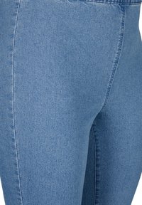 Vaqueros de mezclilla elástica azul claro con textura suave, cintura alta y detalles cosidos a lo largo de las costuras laterales para un ajuste entallado.