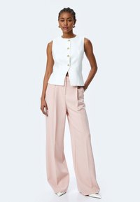 Witte mouwloze blouse met vijf gouden knopen, gecombineerd met roze wijde broek. Gladde stof met een getailleerde pasvorm en een minimalistisch ontwerp.