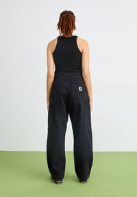 Svart tanktop og løstsittende svarte cargo-bukser med to store baklommer. Materialet ser ut til å være bomull denims. Enkel design, ingen mønstre.