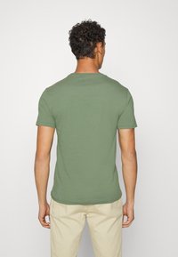 Oliivinvihreä lyhythihainen t-paita, jossa on pyöreä pääntie, sileä koostumus ja rento istuvuus, yhdistetty vaaleisiin housuihin.