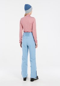 Lange mouwen, lichtroze top met een hoge kraag, gecombineerd met lichtblauwe broek met een geplooide tailleband en uitsparingen bij de enkels. Zwarte laarzen.