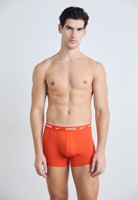 Orange Baumwoll-Boxershorts mit Stretchanteil und einem weißen Nike-Logo am Bund. Die Passform liegt enganliegend am Körper, mit einer glatten Textur und minimalen Nähten.