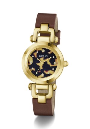 Montre-bracelet ronde Guess dorée avec bracelet en cuir marron, cadran imprimé léopard et index heures en cristal sur fond blanc.