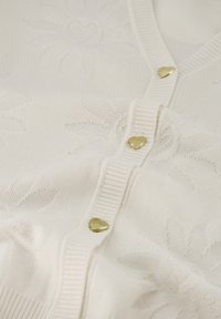 Witte cardigan met een textuurpatroon van bloemen, met ribbelafwerking en gouden hartvormige knopen aan de voorkant. Zachte, gebreide stof.