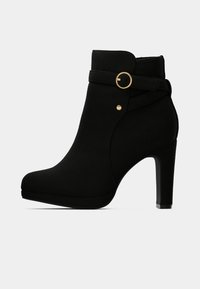 Juodos aukštakulnės aulinės botinės, pagamintos iš minkštos zomšos, su apvalia nosimi, dirželiu su auksiniu apvaliu akcentu ir tekstūruotu paviršiumi.