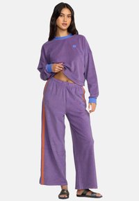 Conjunto de ropa de estar por casa a rayas moradas que incluye un top de manga larga recortado con acentos azules y pantalones de pierna ancha con paneles laterales naranjas.