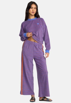 Conjunto de ropa de estar por casa a rayas moradas que incluye un top de manga larga recortado con acentos azules y pantalones de pierna ancha con paneles laterales naranjas.